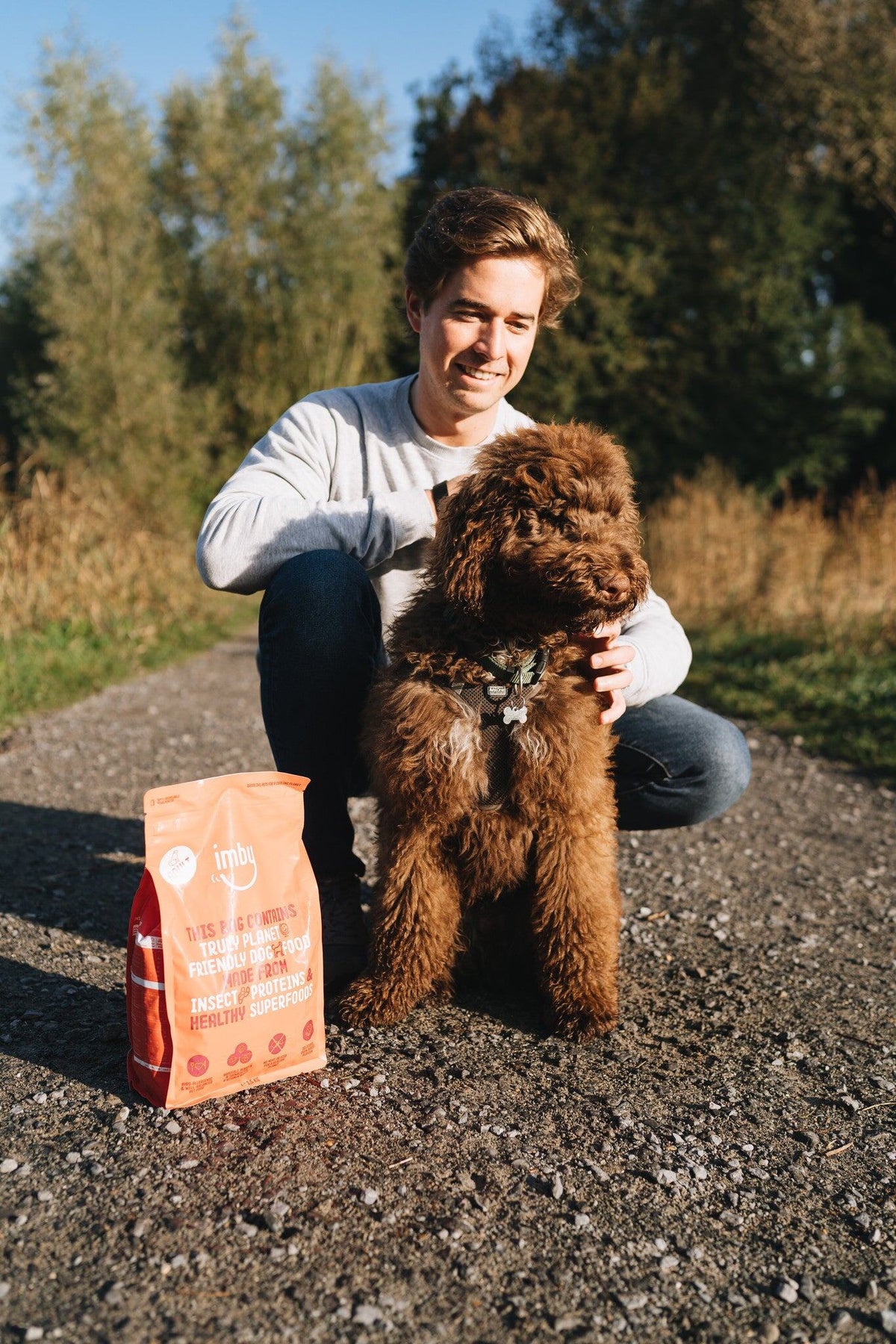 Baasje met bruine krullende hond naast een zak Imby insectenbrokken